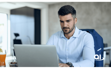 Mann mit hellblauem Hemd und kurzem Bart arbeitet am Laptop an einem Schreibtisch mit Orangensaft und Snacks.