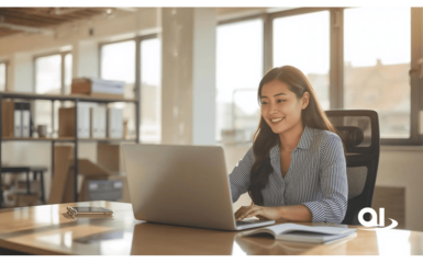 Woman in a striped shirt sits at a desk in a bright office and types on a laptop.