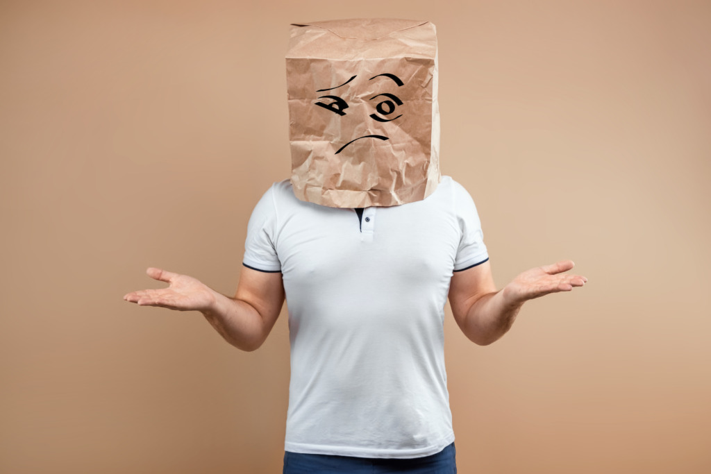 The man put a paper bag on his head, spreads his arms to the sides, despondency, depression. Isolate on yellow background